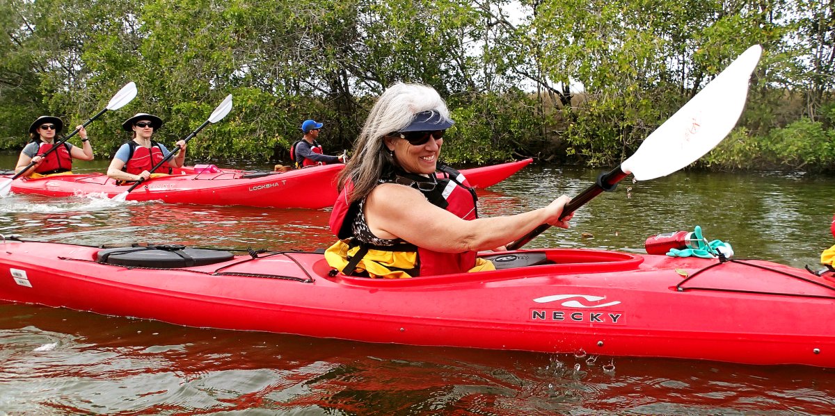 A group of people sea kayaking with the woman in the center of the frame smiling while paddling