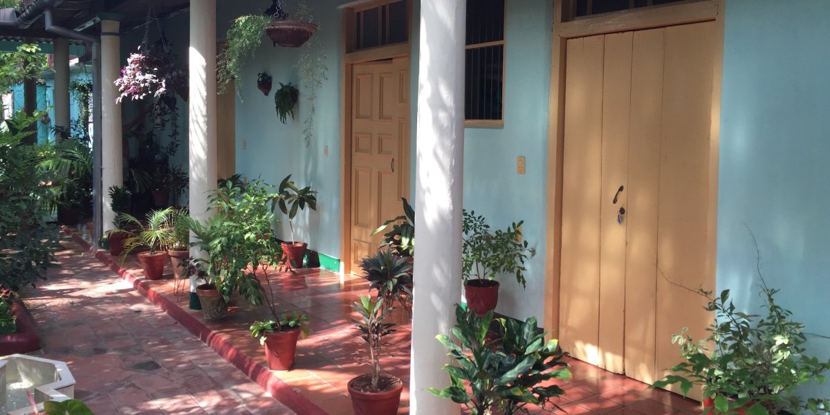 The patio of a Cuban Casa Particular with two yellow doors going to rooms in a blue building