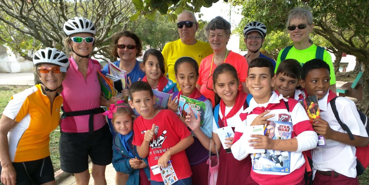 A group of cyclists on tour in Cuba smiling with Cuban kids at a school