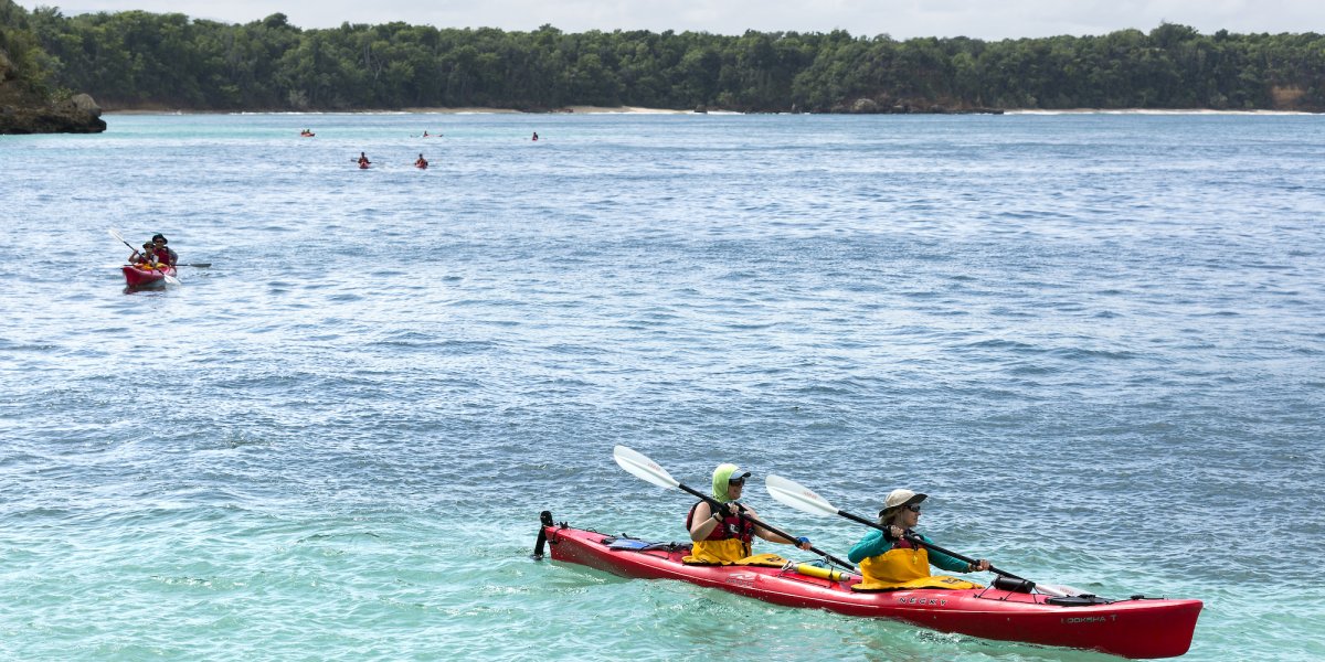 A group of people Sea Kayaking in Cuba in red tandem sea kayaks on warm turquoise blue Caribbean waters.