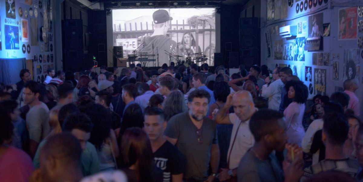 People dancing with a big electronic screen showing a black and white film at a night club in Havana, Cuba