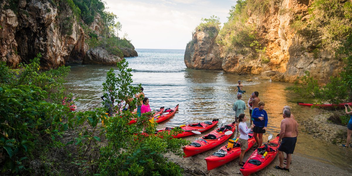 A group of people standing around their sea kayaks in a small cove off of Guajimico, Cuba.