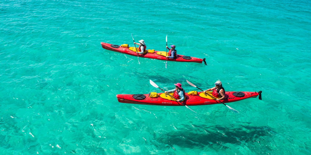Two red tandem sea kayaks atop crystal clear turquoise water in the Caribbean.