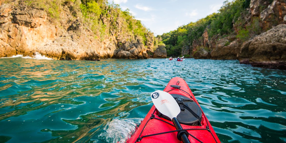 The front of a red kayak on the water in Cuba with sandstone cliffs in the background