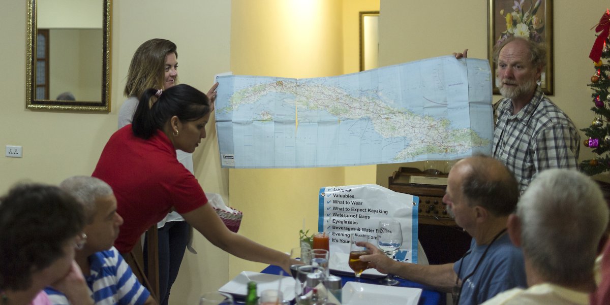 Two people holding up a map of the island of Cuba with a table of people looking at it