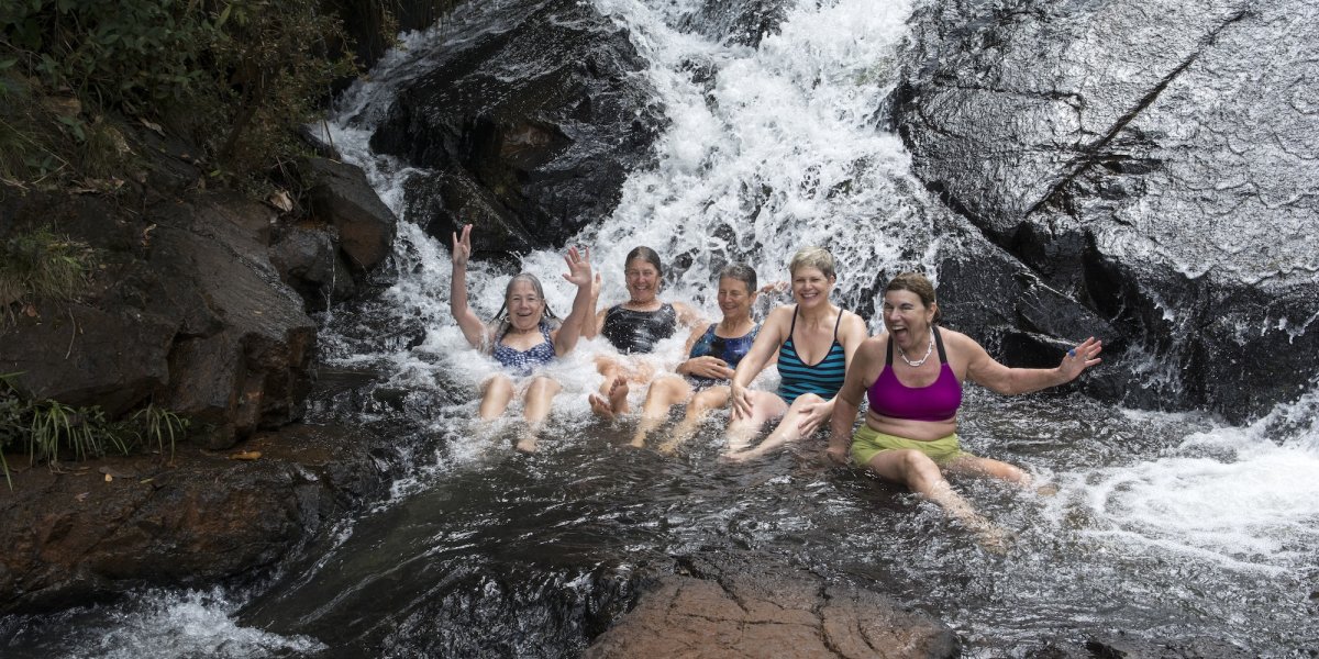 Group of women laughing and relaxing under a waterfall in Cuba, a refreshing and joyful experience on adventurous trips to Cuba.