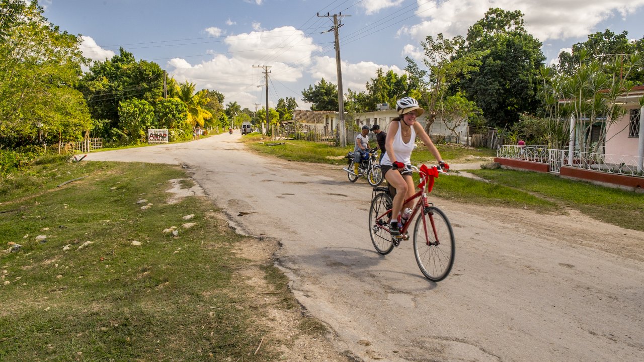 A woman smiling while riding her bike on a paved road in Cuba