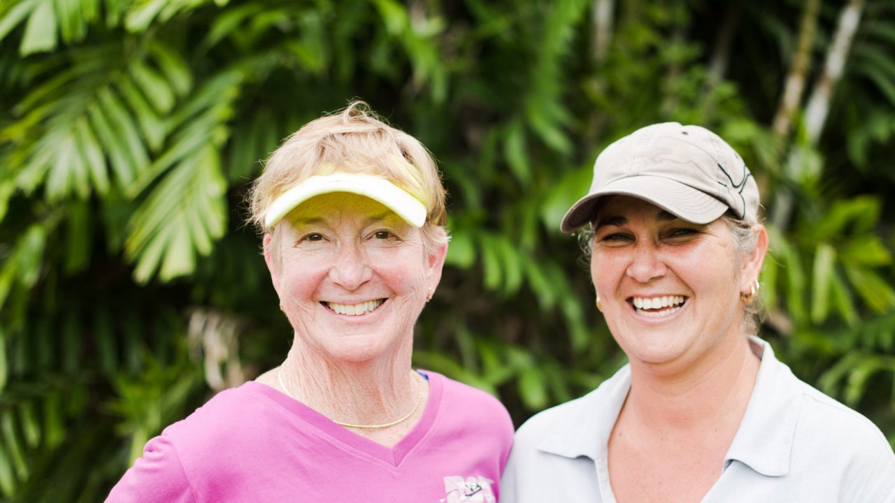 Two women smiling in front of a green landscape in Cuba during a walking tour.
