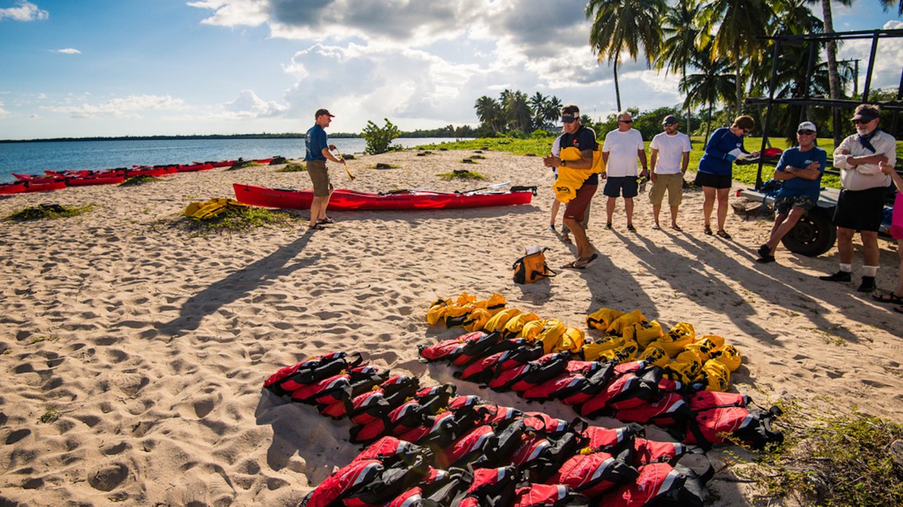 Life jackets and sea kayaks scattered across the beach with people lined up to get gear