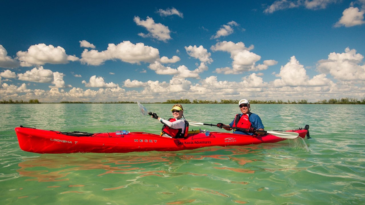 Two people in a sea kayak in Cuba paddling over the clear water.