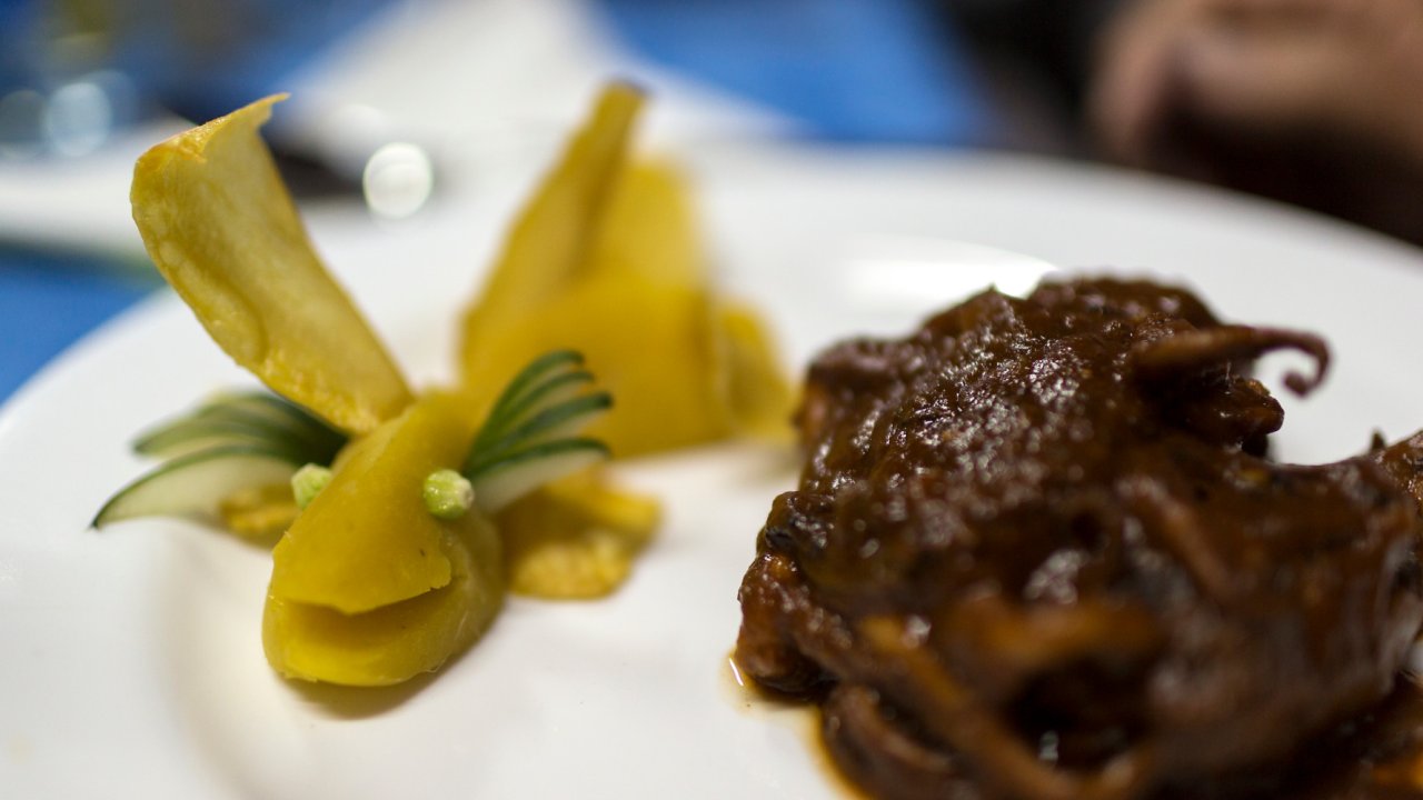 A white dinner plate with some kind of meat on the right and pickled vegetables plated to look like a fish on the left