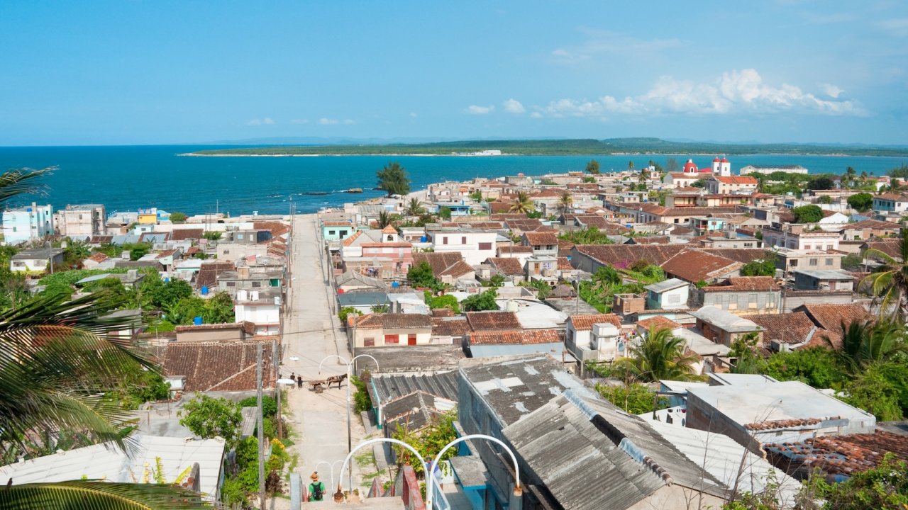 Scenic coastal view of Gibara, Cuba with oceanfront homes, palm trees, and the turquoise Caribbean Sea in the background.