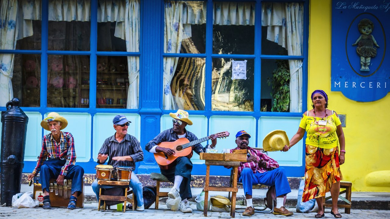 A group of local cubans sitting outside a blue building playing various instruments