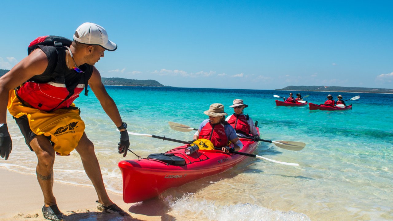 A red tandem kayak being pulling onto the shore by a local your guide in Cuba