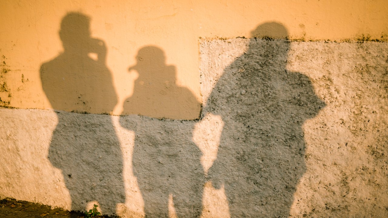 The shadow of three people all taking pictures against a wall at golden hour