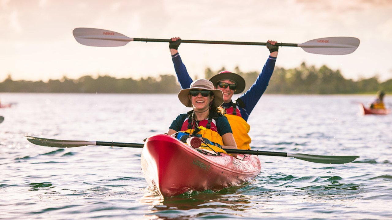 Two people in a red tandem kayak holding up their paddles and smiling