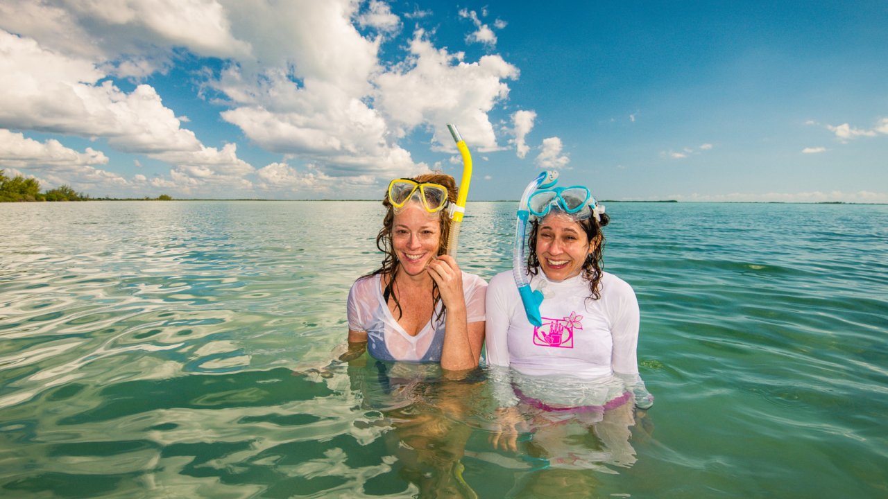 Two women standing up in the Caribbean with their snorkels on their head smiling