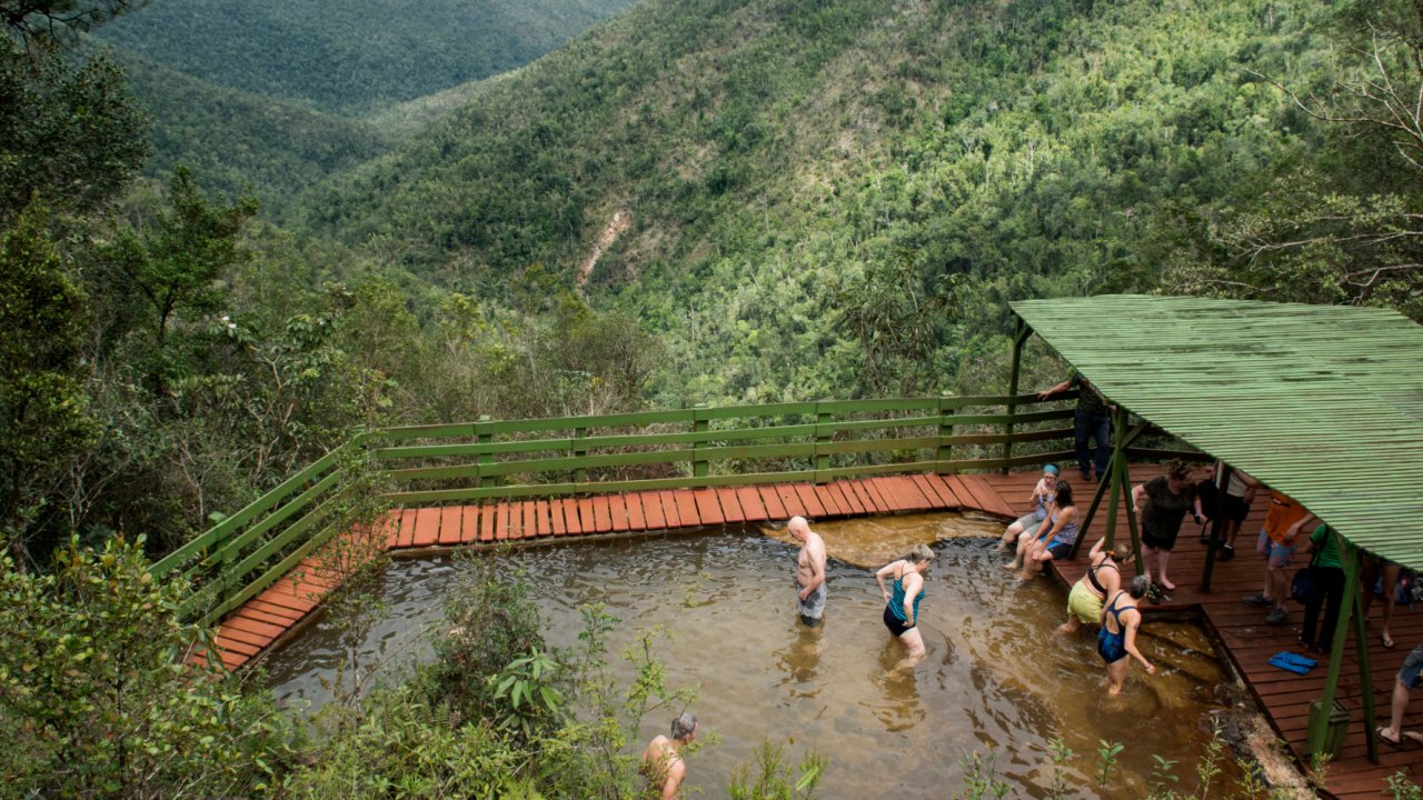 A group of tourists soaking in a hot spring among rolling green hills in Cuba