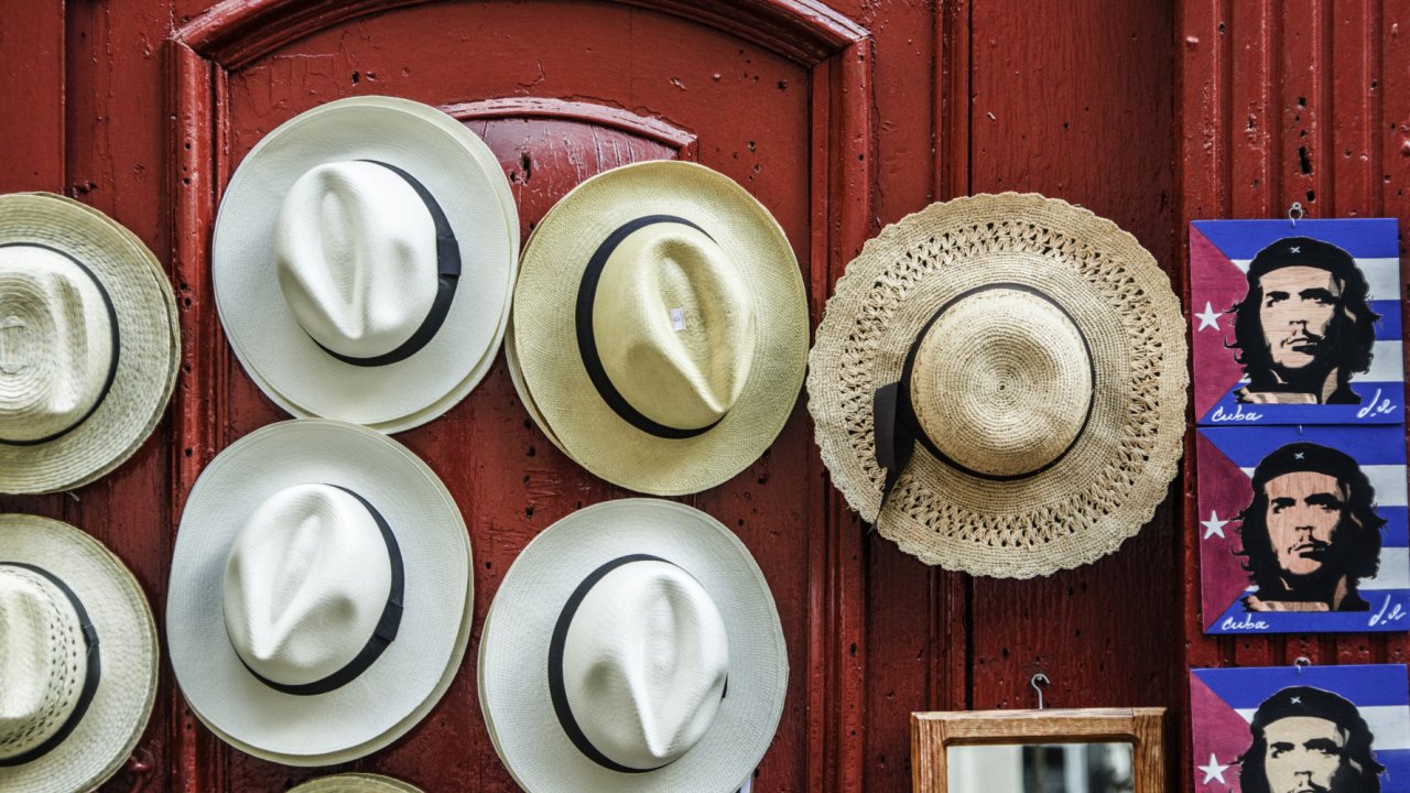 A series of sun hats hung on a door next to a row of stickers of the Cuban flag