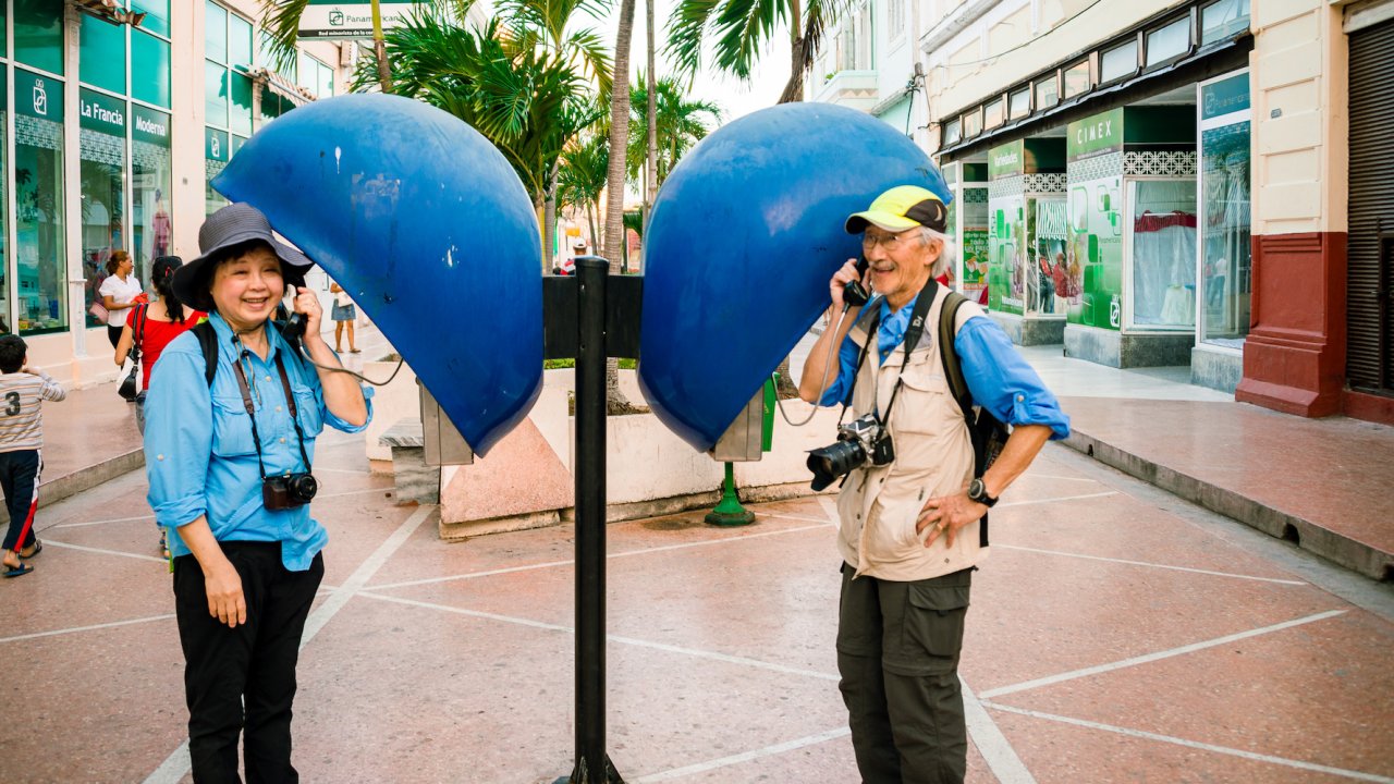 Two tourists with camera around their necks pretending to be on the phone with each other