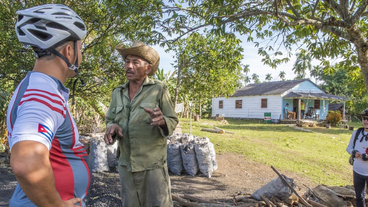 A Cuban farmer talks to cyclists in a rural village, offering an authentic cultural experience during a bicycle tour of Cuba through scenic countryside routes.