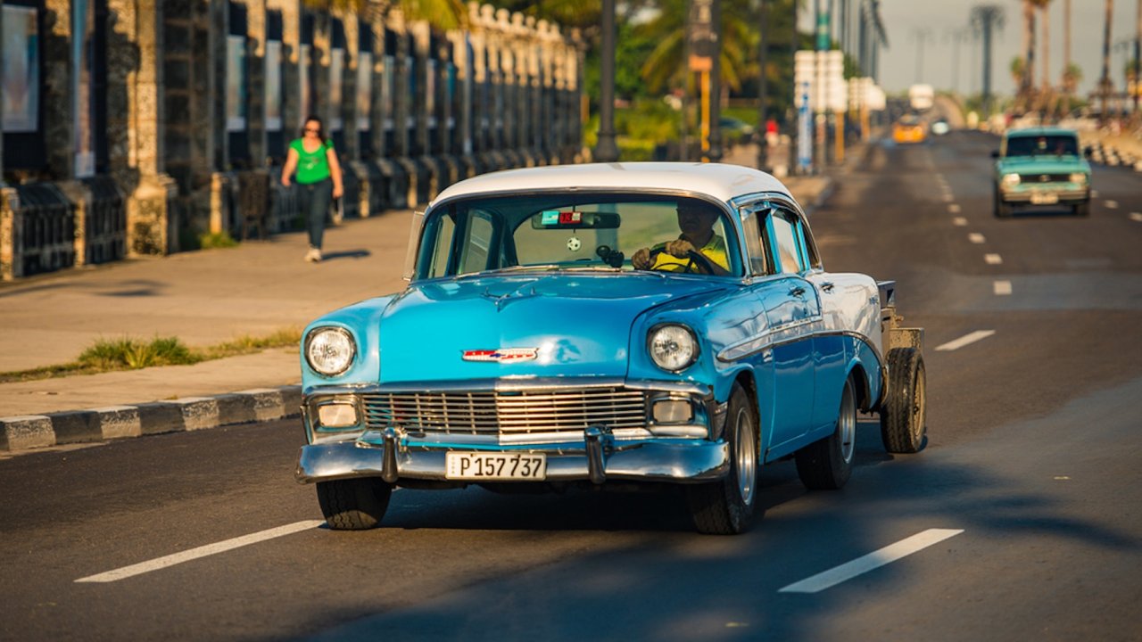 A vintage blue car drives along Havana’s Malecón, one of the city’s most iconic spots to visit during a weekend in Havana travel tour from the US.