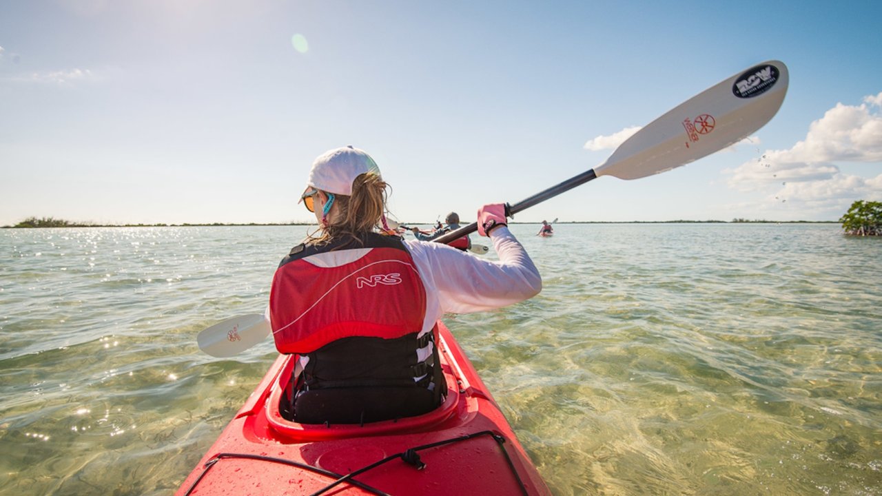 A woman sea kayaking through clear water on a sunny day in Cuba.