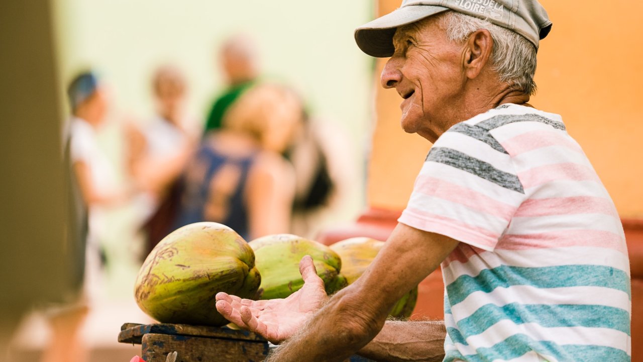 Local Cuban street food vendor selling fresh coconuts during a Havana day tour, with tourists in the background.
