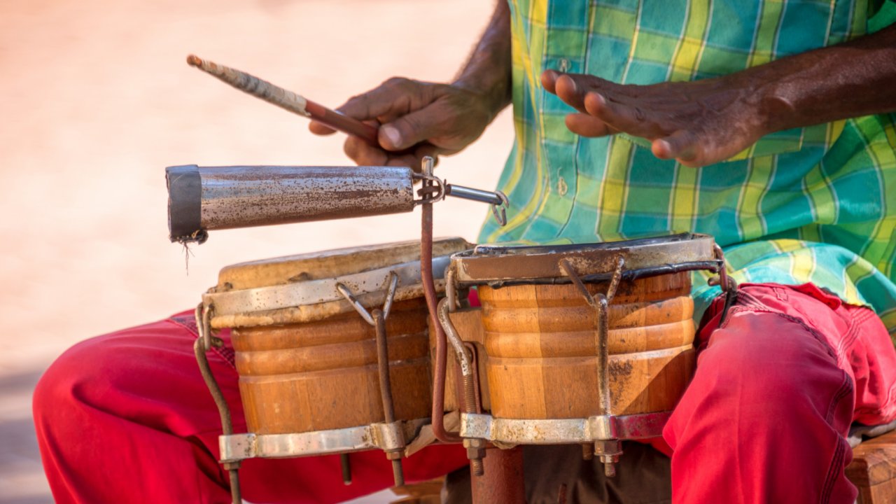 A man holding one drum stick while playing a set of bongos