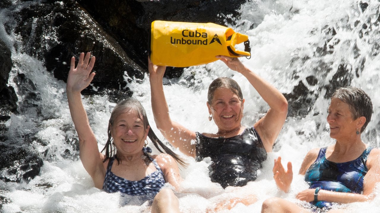 Travelers cooling off beneath a waterfall in Eastern Cuba, enjoying an outdoor adventure during a Cuba Unbound excursion.