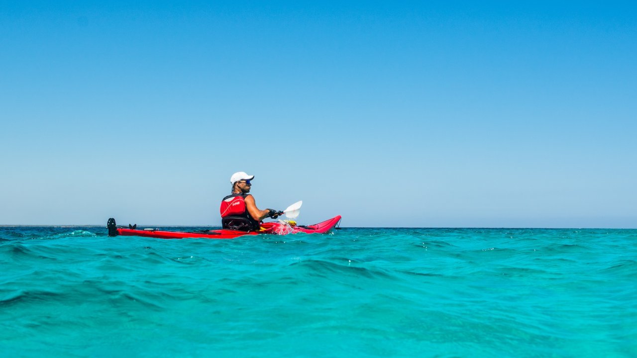 Sea kayaker paddling through turquoise Caribbean waters off the coast of Eastern Cuba under a clear blue sky.