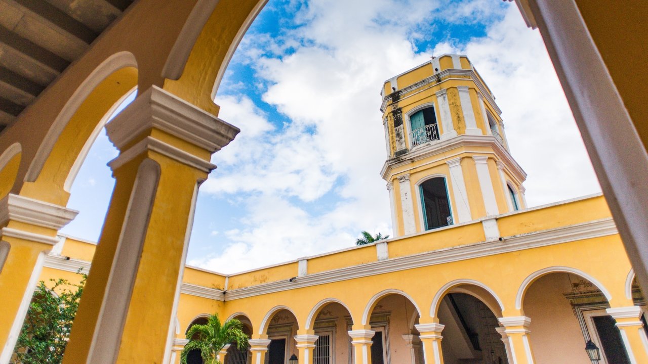 View of Havana’s colorful colonial architecture and bell tower framed by arches, showcasing the city’s charm and history on a weekend in Havana travel tour.
