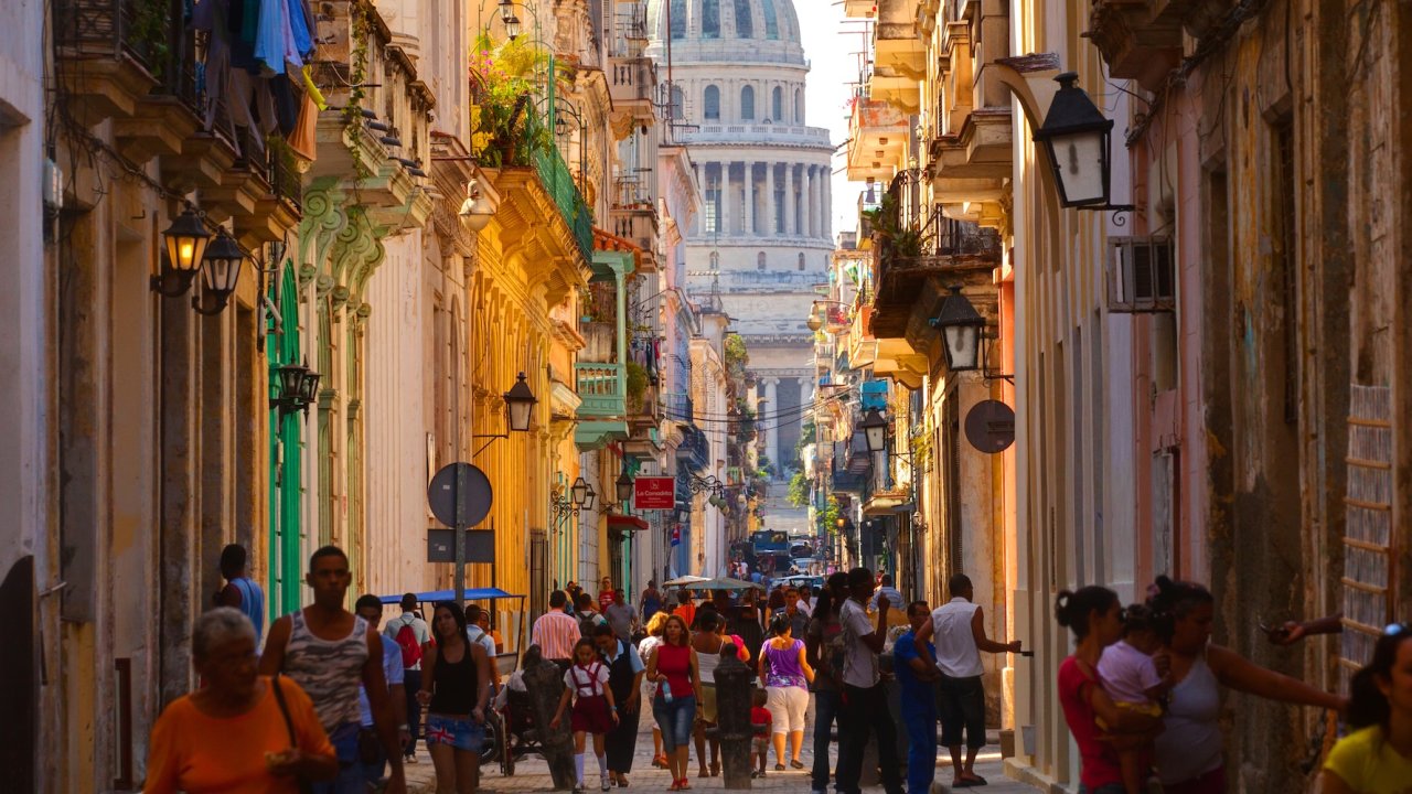 A colorful and bustling street in Old Havana, with locals and tourists walking toward El Capitolio during a Havana day tour.
