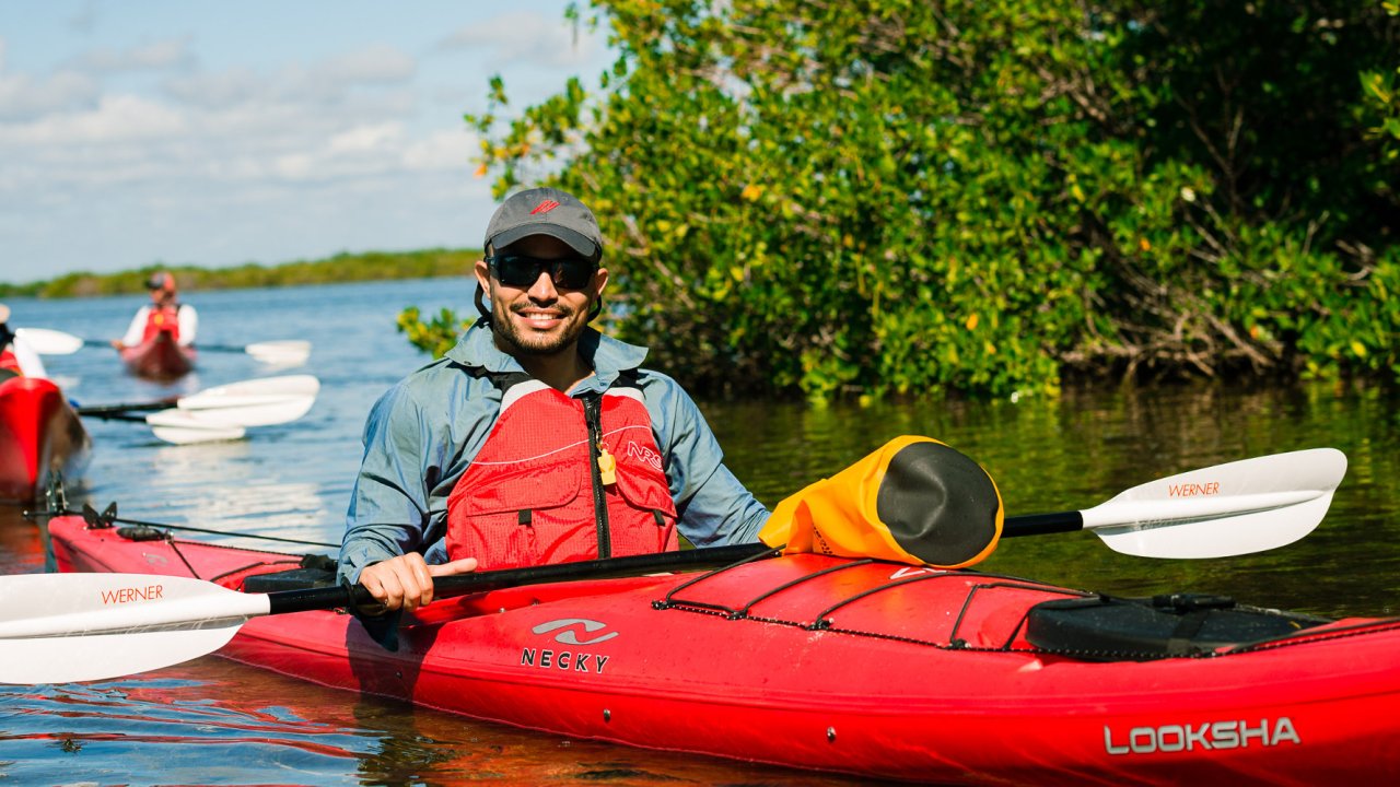 Person in a single kayak with an orange dry bag with mangrove trees behind him in Cuba
