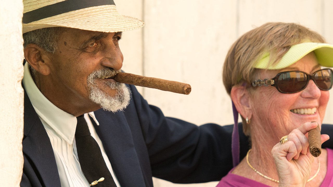 A Cuban man and an American woman smiling while smoking a cigar in Cuba.