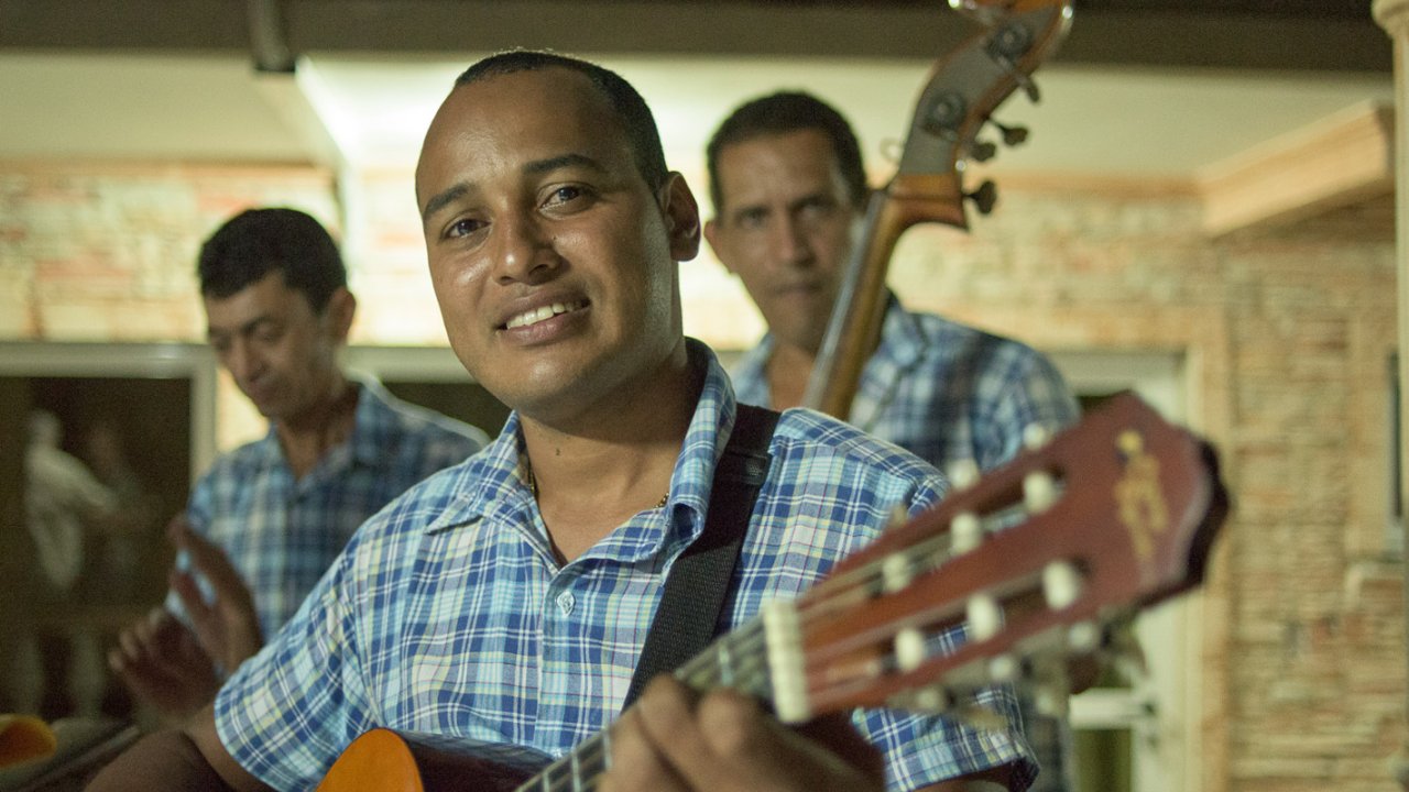 A man holding a guitar and smiling for the camera while playing a show in Cuba