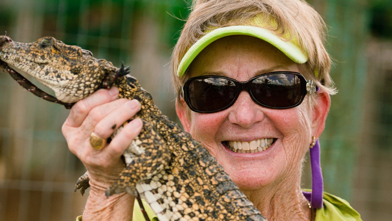 Close up of a woman with a lime green visor holding a small crocodile while on vacation in Cuba.