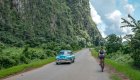 A person biking on a road next to a classic blue Cuban car