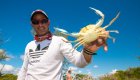A local Cuban man holding a crab in his left hand with blue skies in the background