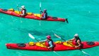 Birds eye view of two tandem red sea kayaks with paddlers atop crystal clear turquoise water in Cuba