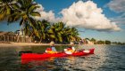 Two people sea kayaking in Cuba along vibrant rocky cliffs and turquoise waters, exploring the coastline near tropical beaches.