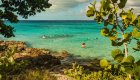 Snorkelers floating in clear turquoise water just off a rocky Cuba beach on the Caribbean coast.