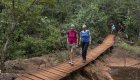 Two women walking across a suspension bridge in a lush forest in Cuba