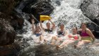A group of tourists sitting at the bottom of a waterfall while one holds up their Cuba Unbound branded dry bag all smiling 