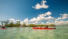 Red sea kayaks gliding across a quiet bay at sunrise on a guided Cuba sea kayaking tour.
