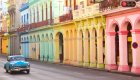 Classic old Cuban car driving past colorful colonial buildings in Havana, Cuba, under warm sunset light—a snapshot of Havana street life.
