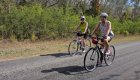 Two women enjoy a sunny day riding road bikes along a quiet highway surrounded by nature during a cycle Cuba tour designed for active travelers.