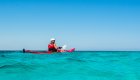 Sea kayaker paddling through turquoise Caribbean waters off the coast of Eastern Cuba under a clear blue sky.
