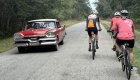 Group of travelers cycling on a quiet road during a Cuba bike tour, passing classic cars and lush landscapes on a guided Cuba tour