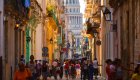 A colorful and bustling street in Old Havana, with locals and tourists walking toward El Capitolio during a Havana day tour.